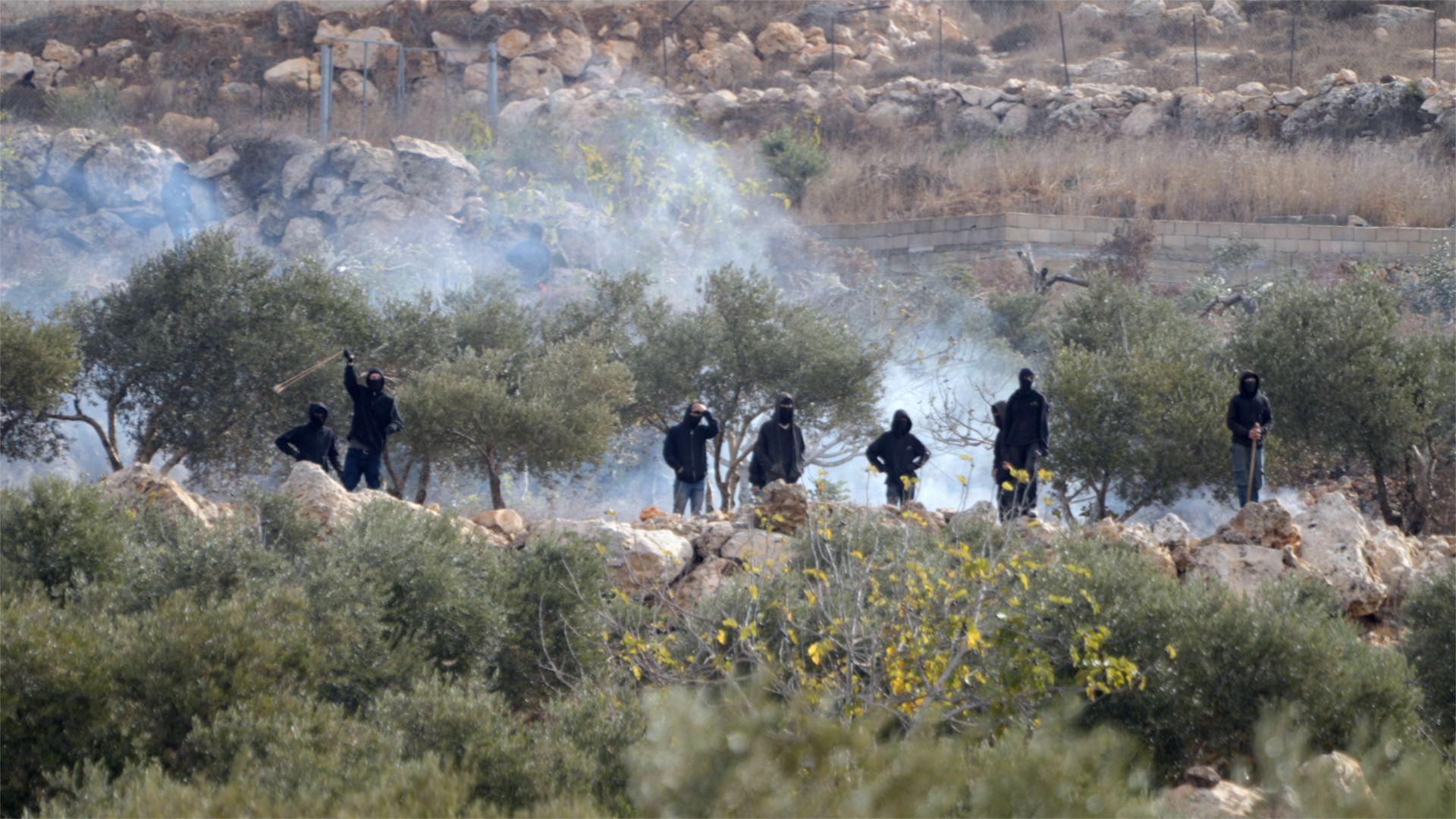 Israeli settlers stand near a fire amid clashes during olive harvest in Abu Falah