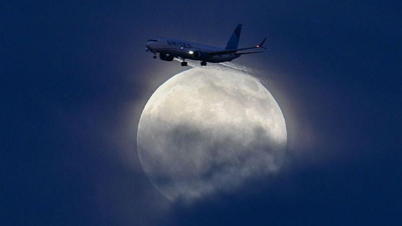 A glowing white moon rising over San Francisco Bay as a plane flies above